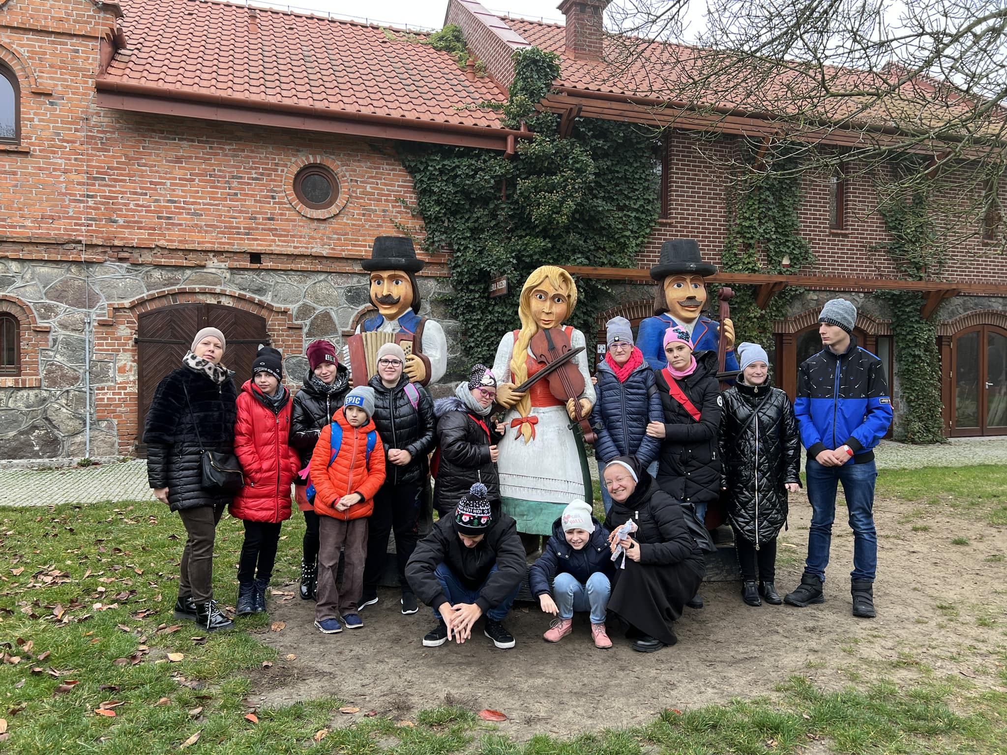 Uczestnicy wyjazdu edukacyjnego przed drewnianą figurą znajdujacą się przy Muzeum w Sierpcu